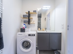 Ein kleines Badezimmer mit Waschmaschine, Waschbecken und Spiegel.