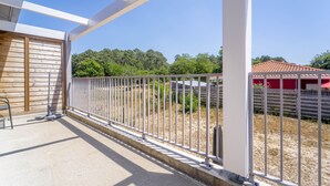 Ein Balkon mit Metallgeländer, einem Betonboden und Blick auf einen eingezäunten Bereich mit Bäumen und einem roten Gebäude im Hintergrund.