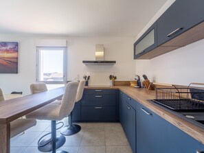 A modern kitchen with a dining area, featuring a wooden table, bar stools, and a built-in stove. - Modern apartment with balcony - 4 guests (Mimizan)