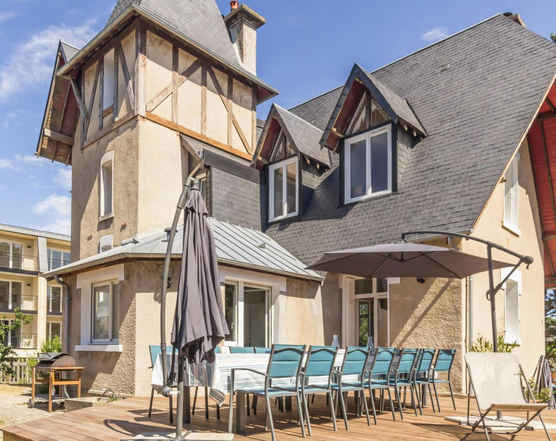 Ein zweigeschossiges Haus mit einer Terrasse, die einen Tisch, Stühle, einen Grill und einen Sonnenschirm bietet.