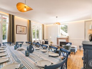 A dining room with a long table set for a meal, a fireplace, and a view through the windows. - Renovated villa with garden - 15 guests (Jullouville)