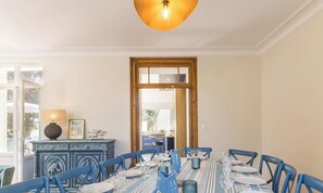 A dining area with a long table set for six, blue chairs, and a decorative cabinet with a lamp. - Renovated villa with garden - 15 guests (Jullouville)