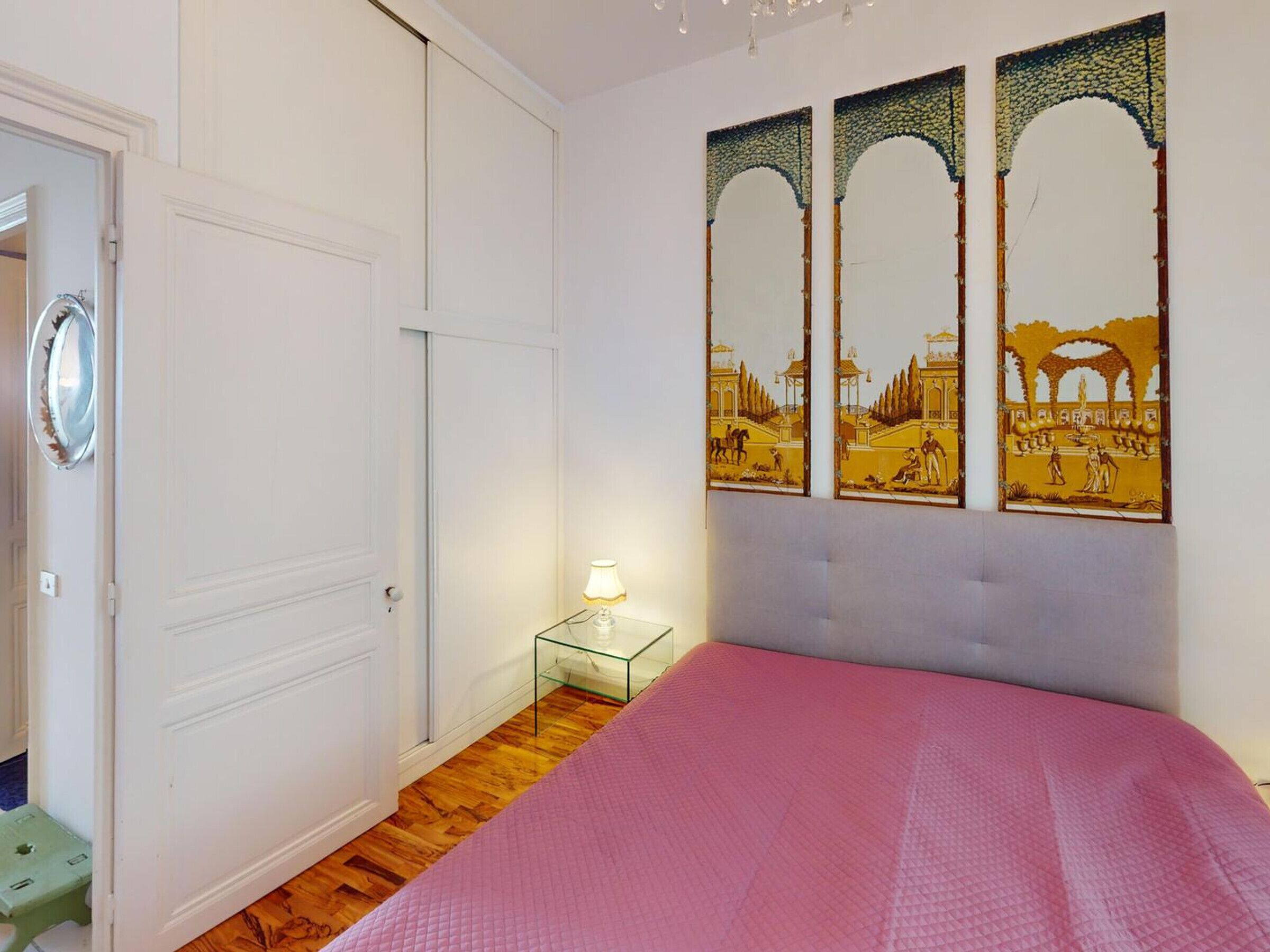 Een slaapkamer met een bed, nachtkastje, lamp en een deur.