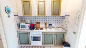 Pieni, käytännöllinen keittiö, jossa on valkoiset kaapit, mikroaaltouuni, kahvinkeitin ja pesuallas.