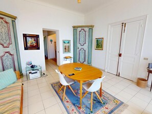 Ein Essbereich mit Holztisch, weißen Stühlen, einem gemusterten Teppich und einer Tür mit dekorativer Verzierungen.