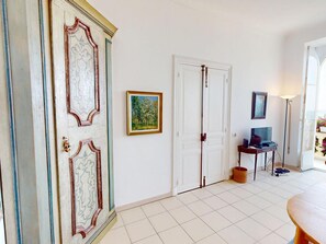 Ein Zimmer mit einer weißen Tür, einem gerahmten Gemälde, einem kleinen Tisch mit Lampe und einem Stuhl.