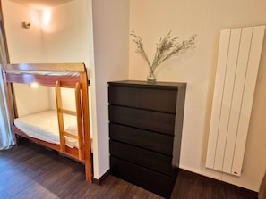 Ein Zimmer mit einem Etagenbett, einem schwarzen Stauraum und einem Heizkörper.