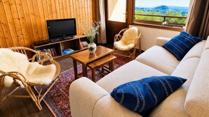 Ein Zimmer mit Fernseher, zwei Stühlen, einem Sofa und einem Fenster mit Bergblick.