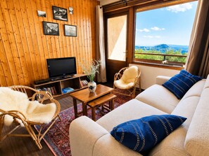 A room with a television, two chairs, a sofa, and a window with a view of mountains. - Bright studio south-facing balcony - 4 guests (Saint-Michel-de-Chaillol)