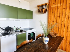 A compact kitchen with a stove, sink, and green cabinets. There's a wooden dining table with chairs and a vase with plants. - Bright studio south-facing balcony - 4 guests (Saint-Michel-de-Chaillol)