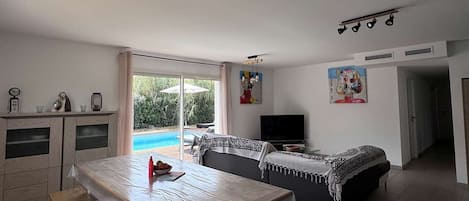 Ein Wohnzimmer mit Blick auf einen Pool, einem Essbereich und einem Fernseher.