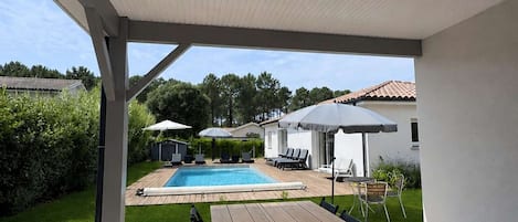 Ein überdachter Außenbereich mit Pool, Liegestühlen und Sonnenschirmen.