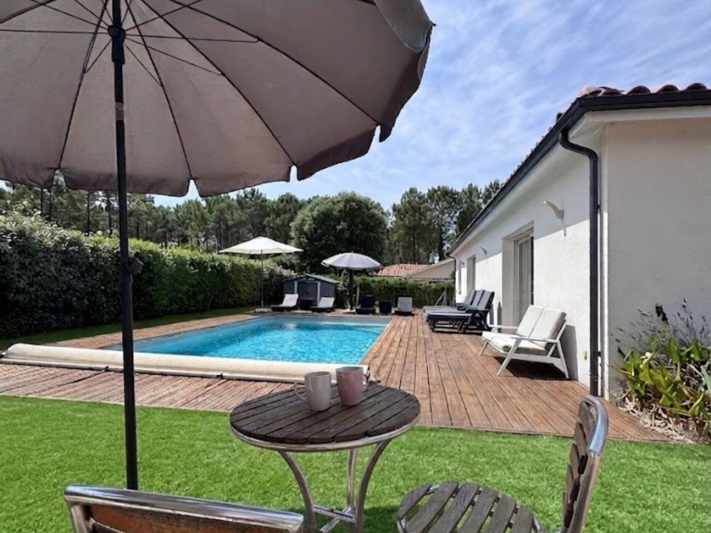 Uma piscina com espreguiçadeiras, uma mesa e guarda-sóis em um quintal.