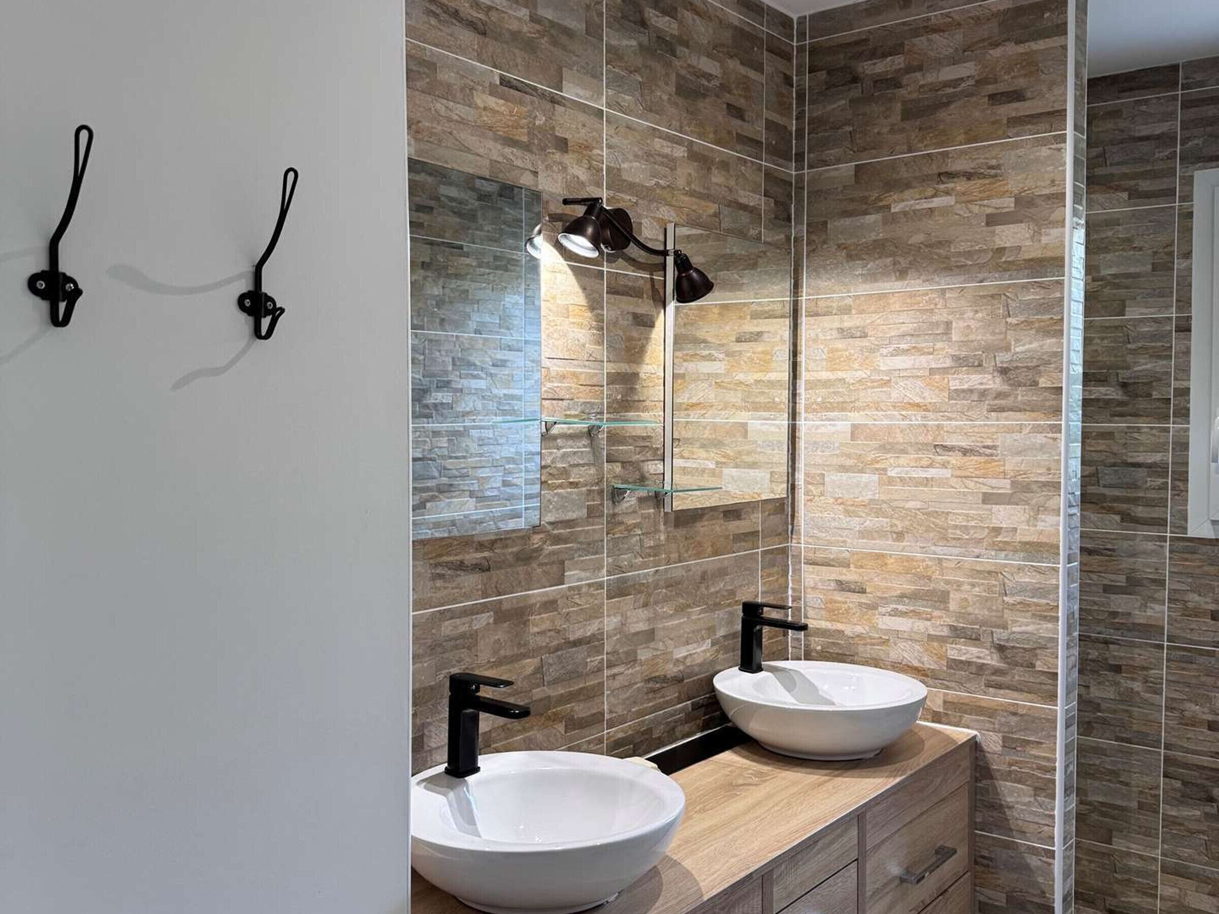 Une salle de bain avec deux lavabos, un miroir et un luminaire fixé au mur.