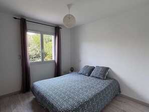 Ein Schlafzimmer mit Bett, Fenster mit Vorhängen, Nachttisch und einer Pendelleuchte.