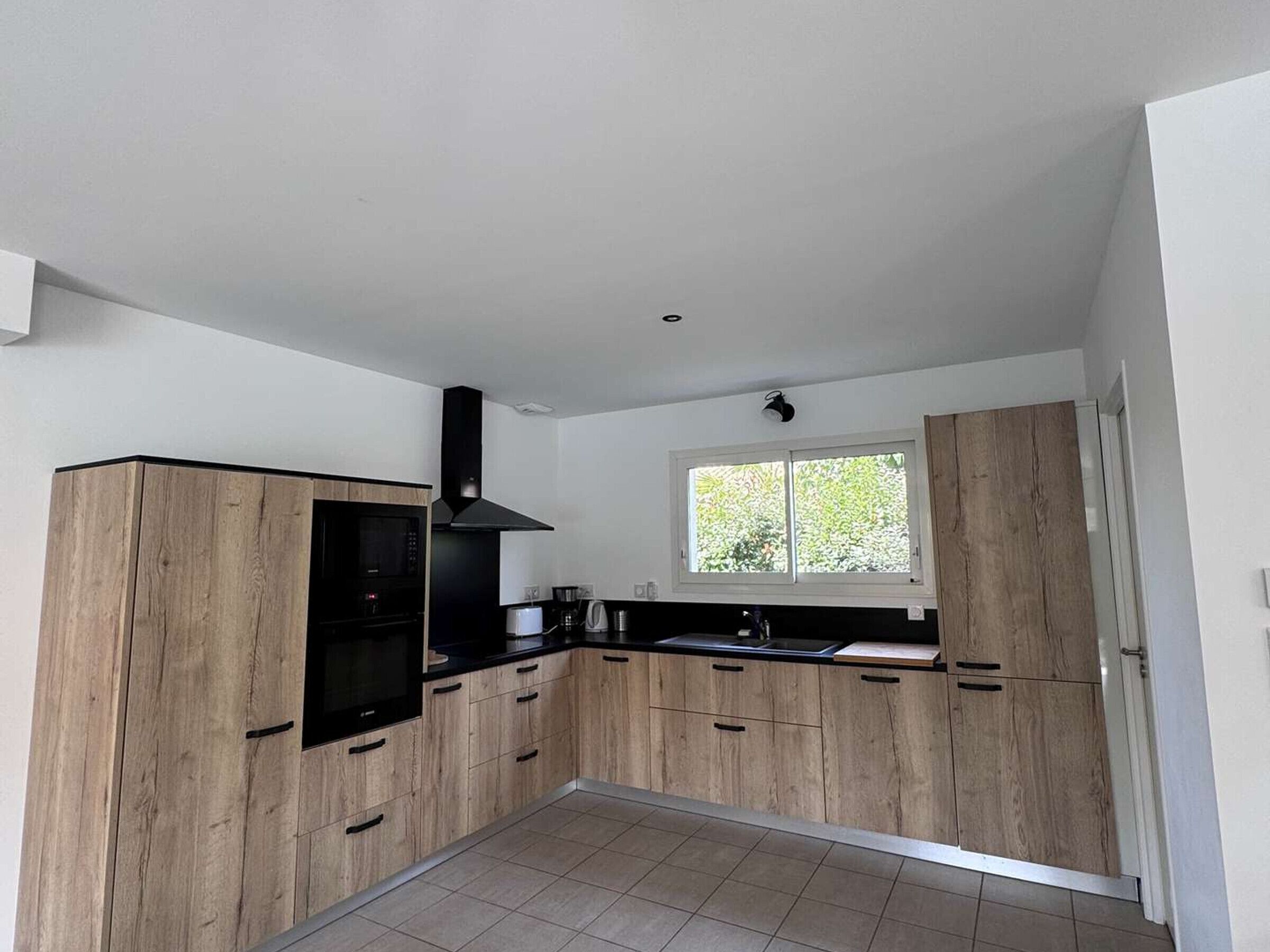 A modern kitchen with wooden cabinets, a black range hood, and a window providing natural light.