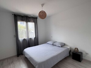 A bedroom with a bed, a nightstand, a lamp, and a window with curtains. - Villa with pool, WiFi - 10 guests (Moliets-et-Maa)
