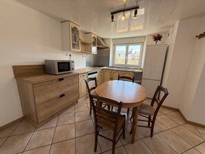 Eine Küche mit einem Holztisch, Stühlen, einer Mikrowelle, Schränken und einem Fenster.