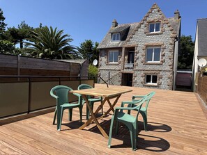 Eine Terrasse mit Holztisch und vier Stühlen, ein Steinhaus im Hintergrund und ein Holzzaun.