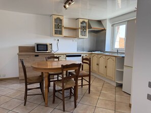 A kitchen with a dining table, chairs, a microwave, and cabinets. - Cozy apartment near beach - 3 guests (Perros-Guirec)