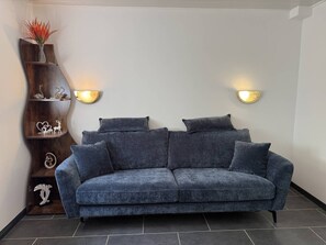 Ein modernes Wohnzimmer mit einem dunkelblauen Sofa, zwei Wandleuchten und einer Holzkommode mit Dekorationselementen.