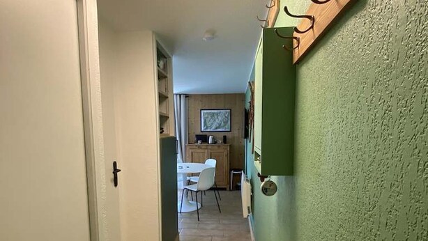 Corredor que dá para uma sala de jantar com mesa e cadeiras, uma área de cozinha com armários e uma parede verde com textura.