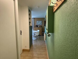 A hallway leading to a dining area with a table and chairs, a kitchen area with cabinets, and a green textured wall. - Cozy apartment in village center - 4 guests (Arêches-Beaufort)