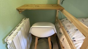 Uma cama beliche com prateleira de madeira acima, uma cadeira branca e um radiador.
