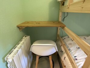 Ein Stockbett mit einem Holzboden darüber, ein weißer Stuhl und eine Heizung.