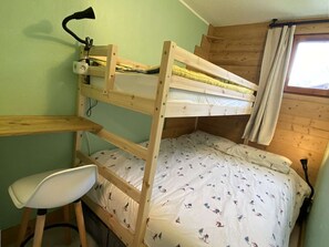 Una cama litera con escritorio y silla, una lámpara y una ventana con cortinas.