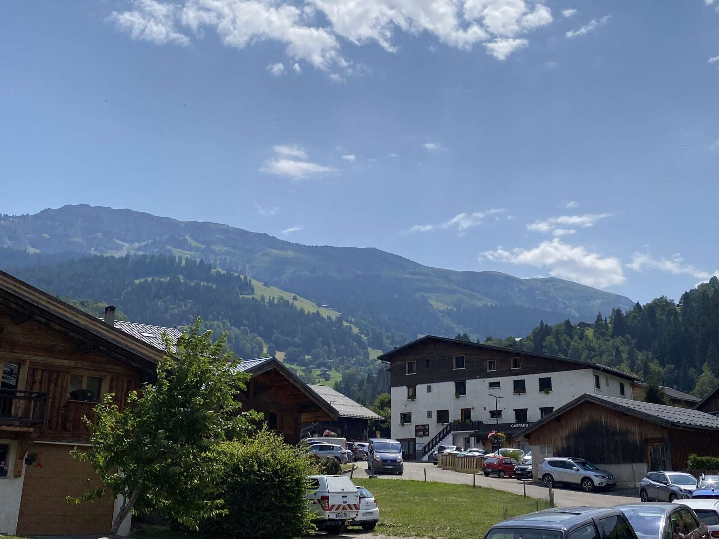 A mountain village with traditional wooden buildings, a parking area, and a view of the surrounding hills.