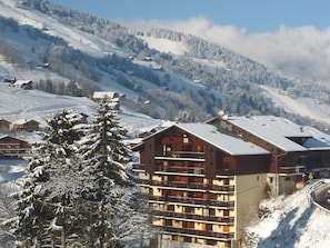 A multi-story building with balconies, surrounded by snow-covered hills and trees. - Cozy apartment in village center - 4 guests (Arêches-Beaufort)