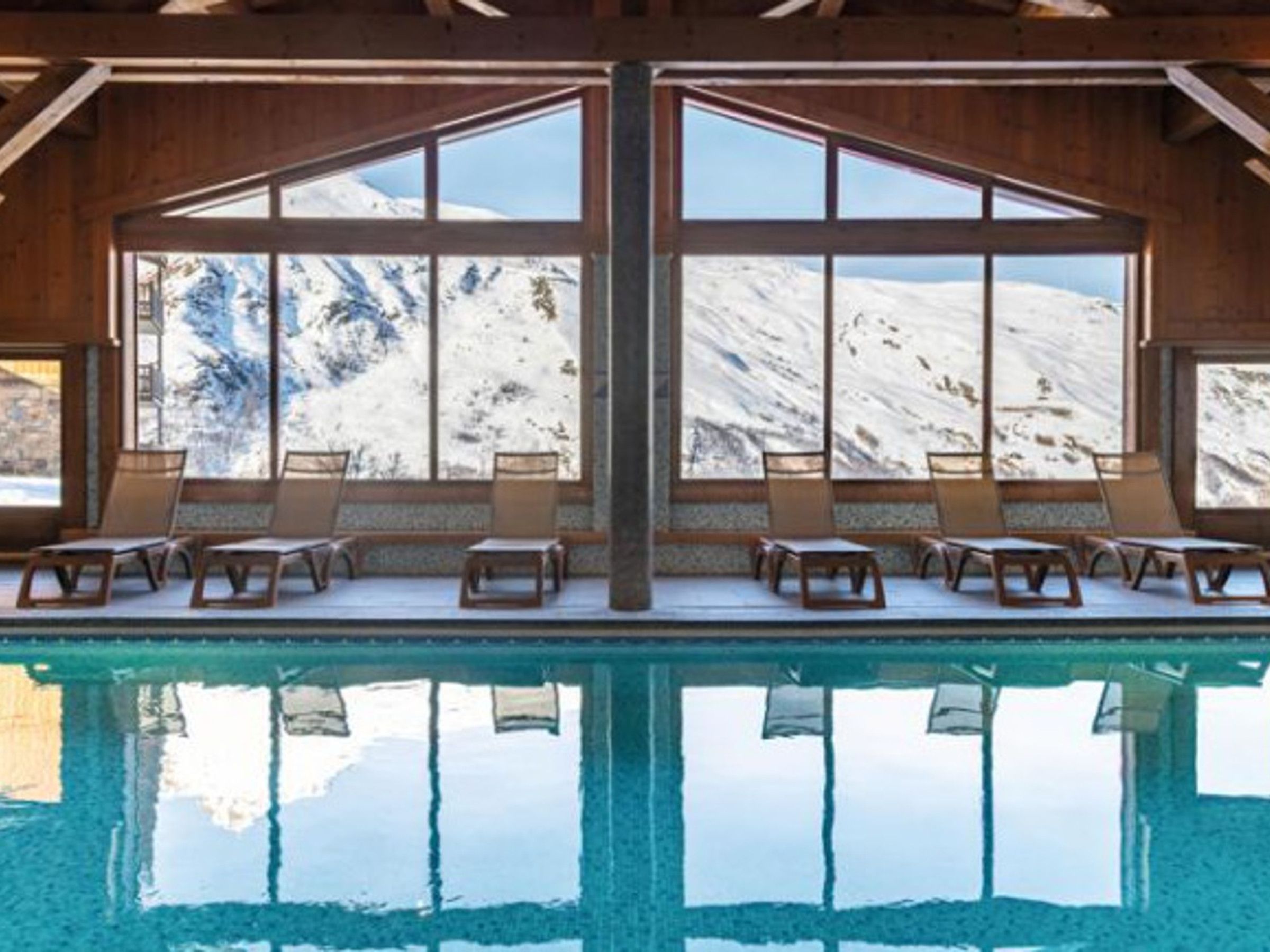 A pool area with lounge chairs and large windows offering a view of snow-capped mountains.