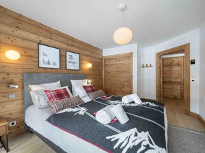 A bedroom with a bed, wooden panel walls, framed pictures, a bedside table, and a door. - Family apartment, ideal location - 4 guests (Méribel)