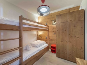 A bunk bed room with wooden walls, a red stool, and a ceiling light fixture. - Family apartment, ideal location - 4 guests (Méribel)