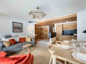 A modern living room with a sofa, a dining table set for two, and a kitchen area with wooden cabinets. - Family apartment, ideal location - 4 guests (Méribel)