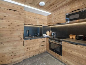 A modern kitchen with wooden cabinetry, a built-in oven, and a stainless steel range hood. - Family apartment, ideal location - 4 guests (Méribel)