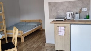 A compact room with a wooden bed, a small kitchenette, a white refrigerator, and a wooden chair. - 4-person Room With Kitchenette, Sarbinowo (Mielno)