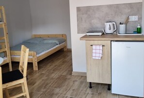 Ein gemütlicher Raum mit einem Holzbett, einer kleinen Küchenzeile, einem weißen Kühlschrank und einem Holzstuhl.