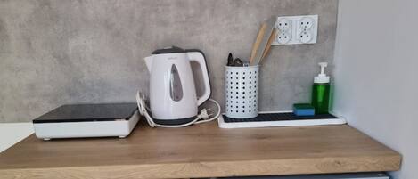 A kitchen counter with a coffee maker, a kettle, a container with utensils, a soap dispenser, and a small refrigerator.