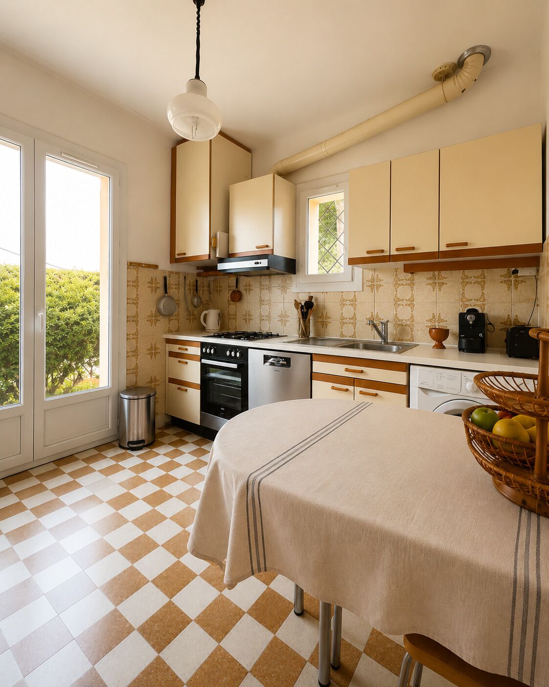 Una cocina con suelo a cuadros, una mesa de comedor con mantel y una ventana con vistas a vegetación.