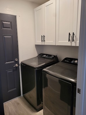 A laundry room with two front-loading washers and dryers, a door, and white cabinets above. - 3 bedroom Oasis, Steps from Glendale Stadium (Phoenix)