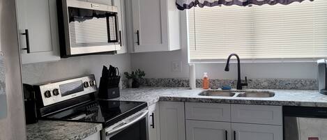 A kitchen with white cabinets, a microwave, an oven, a sink, and a window with blinds.