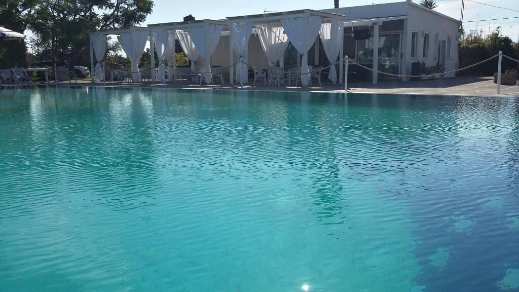 A clear blue pool with white canopies and lounge chairs.