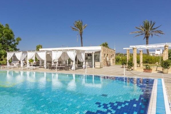 A swimming pool with a clear blue water surface, surrounded by white canopies and palm trees.