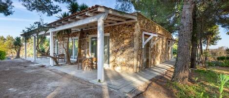 A stone building with a pergola, outdoor seating, and a dirt path.