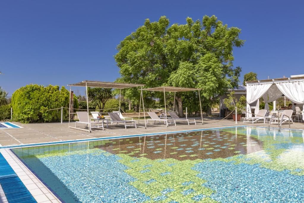 Piscina com espreguiçadeiras e guarda-sóis, cercada por vegetação e árvores.