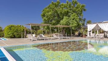Piscina com espreguiçadeiras e guarda-sóis, cercada por vegetação e árvores.