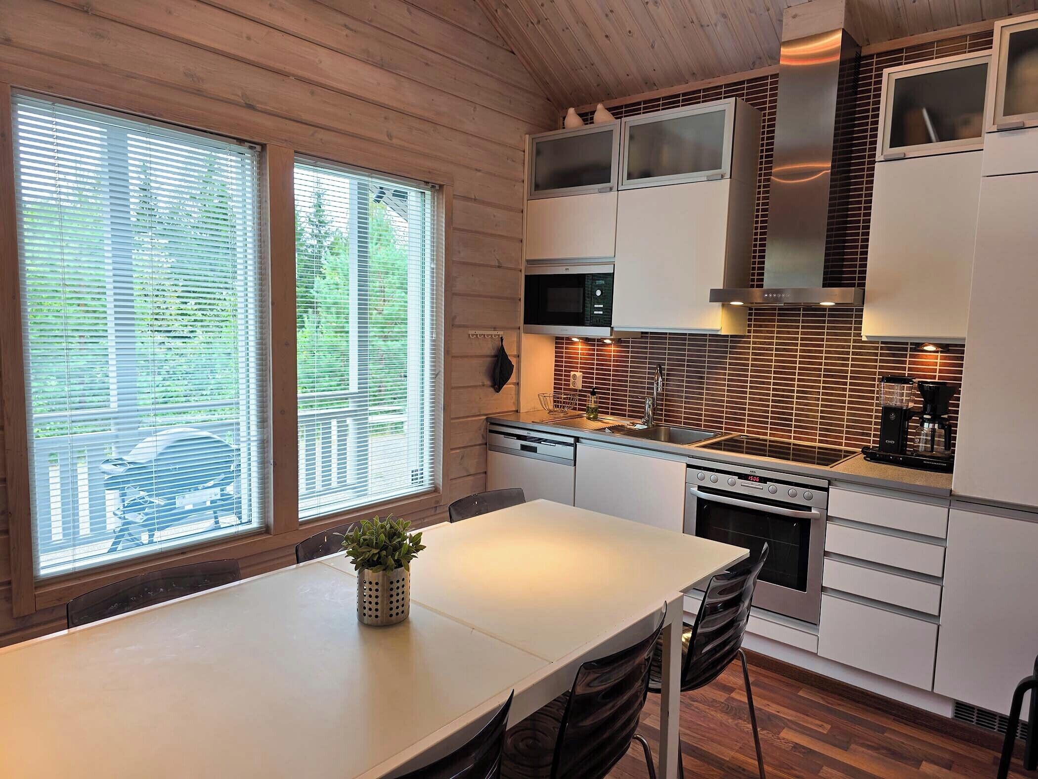 A modern kitchen with a white countertop, stainless steel appliances, and a large window with blinds.