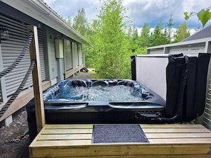 A hot tub with a wooden deck and a metal grate, surrounded by a wooden fence and trees.